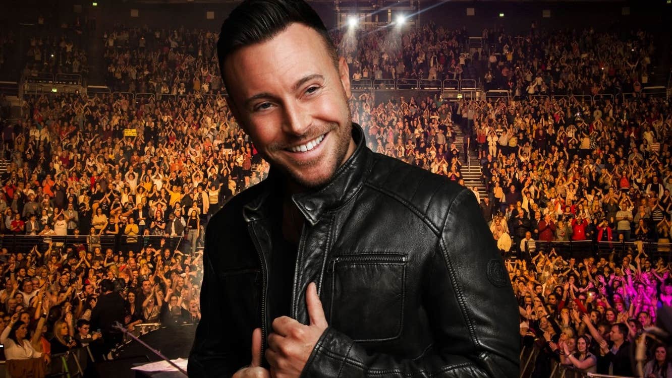 A smiling man in black leather jacket with large audience in the background.
