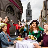 Two people sitting at a table on a street surrounded by actors in costume