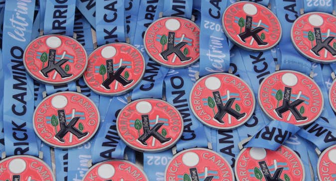 Lots of round red medals with logo for Carrick Camino on and blue ribbons