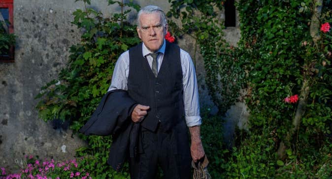 The Man In The Woman’s Shoes at Backstage - a grumpy looking man in shirt and tie holding a jacket in one hand and an old shoe in the other.