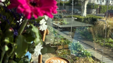 A cup of coffee on a table with a pink flower