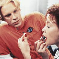 A man looking at a woman putting on lipstick.