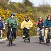 A group cycling on a country road with colourful bushes in the background