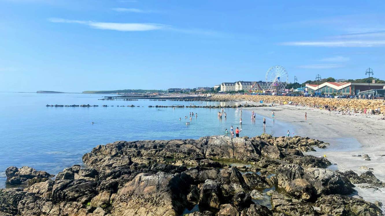 View from the rocks towards a beach with a town and ferris wheel in the background