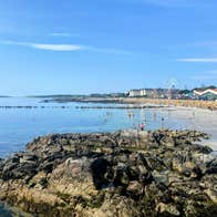 View from the rocks towards a beach with a town and ferris wheel in the background