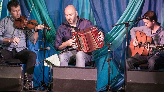 Joyce Brothers Music Festival 2026, 3 seated musicians playing instruments on a small stage area.