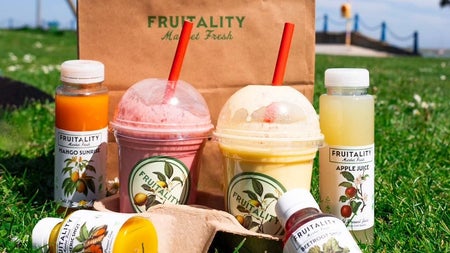 A selection of bottles and containers with colourful fruit juices displayed on grass