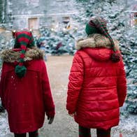 Rear view of 2 children in red coats walking with snow covered christmas trees