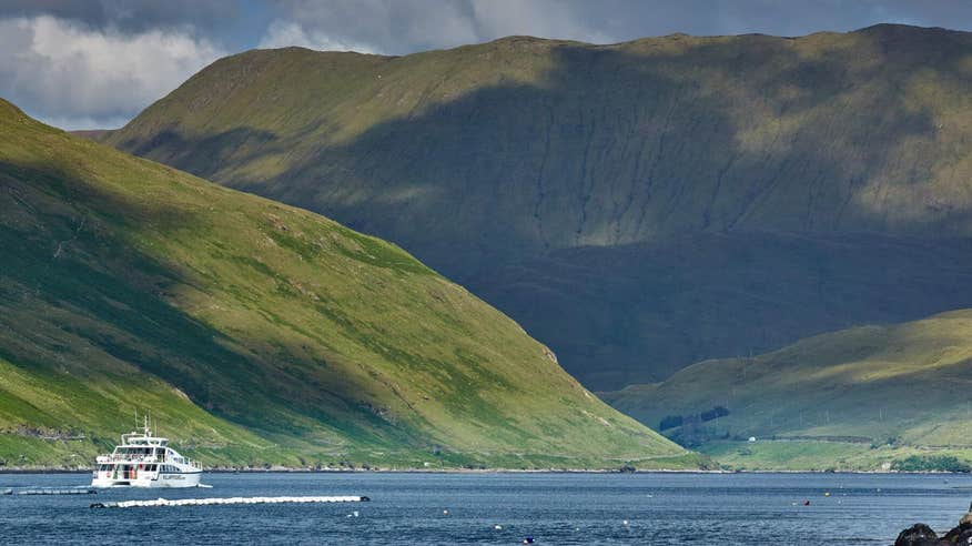 A boat sailing across the water at Killary Harbour with mountains looming in the background