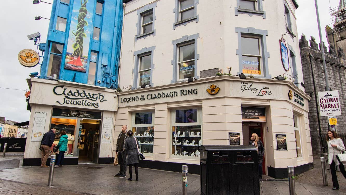 A cream coloured three storey building and shopfront of Claddagh Jewellers on a busy street