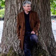 John Spillane standing against a tree by a river.