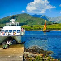 White boat docked at a slipway with green mountains in the background
