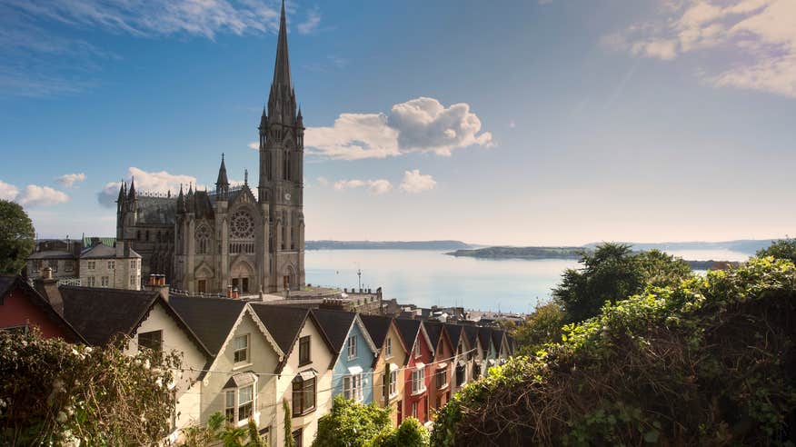 A row of colourful houses with St Colman's Cathedral in the background in Cobh, County Cork