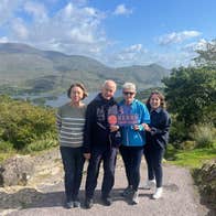 Four people on a path holding a sign with lakes and mountains in the background