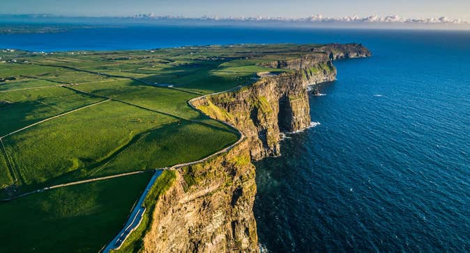 Steep coastal sea cliffs overlook the Atlantic Ocean bordered by green fields and walking paths