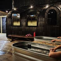 Two people sitting in cold plunge baths with mobile saunas to the right