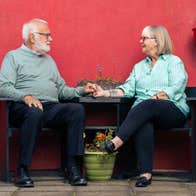 A man and woman seated on dark seats looking at each other, holding hands.