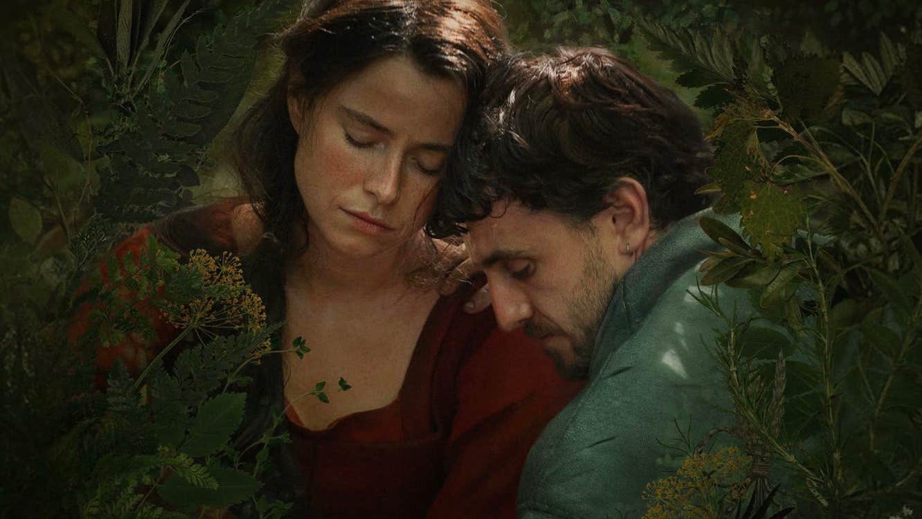 A man and a woman are embracing amongst plants.