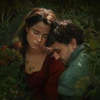 A man and a woman are embracing amongst plants.