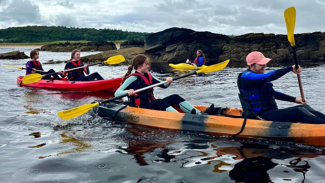 Three kayaks with kayakers and guide on water