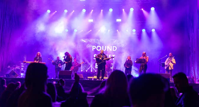 View of a band playing on a stage with purple and white lights.