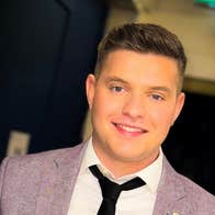 A smiling man in black tie and light grey jacket.