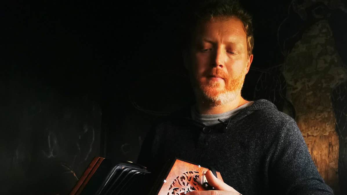 Cormac Begley - Gleneagle, a man looking down at a small hand accordion he is playing.