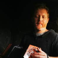Cormac Begley - Gleneagle, a man looking down at a small hand accordion he is playing.