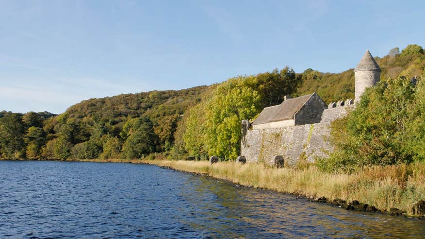 A castle at the side of a lake surrounded by forest