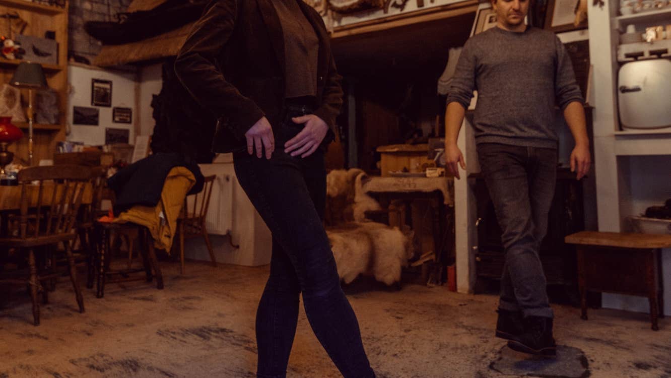 Two people practising Irish dancing in a room with a wooden floor and table and chairs in the background