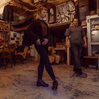 Two people practising Irish dancing in a room with a wooden floor and table and chairs in the background