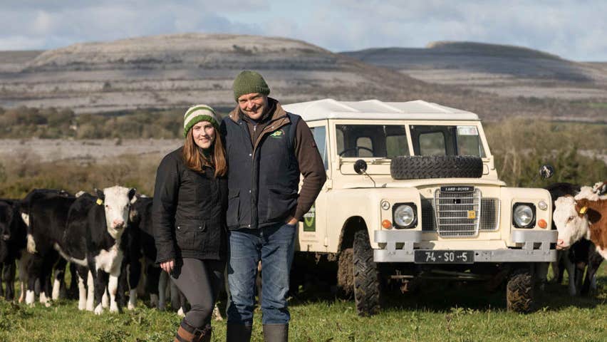 Couple in field with cows and jeep with mountain view