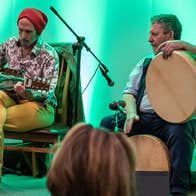 2 seated men with musical instruments on a small stage.