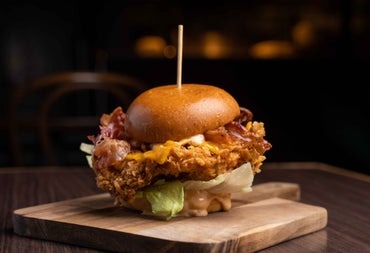 Burger with a large cocktail stick through it on a wooden serving tray 