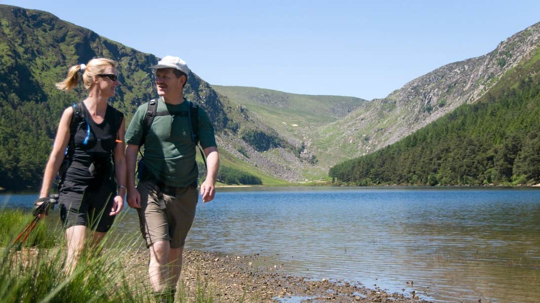 Two people walking beside a lake in Glendalough, Wicklow Mountains National Park, County Wicklow