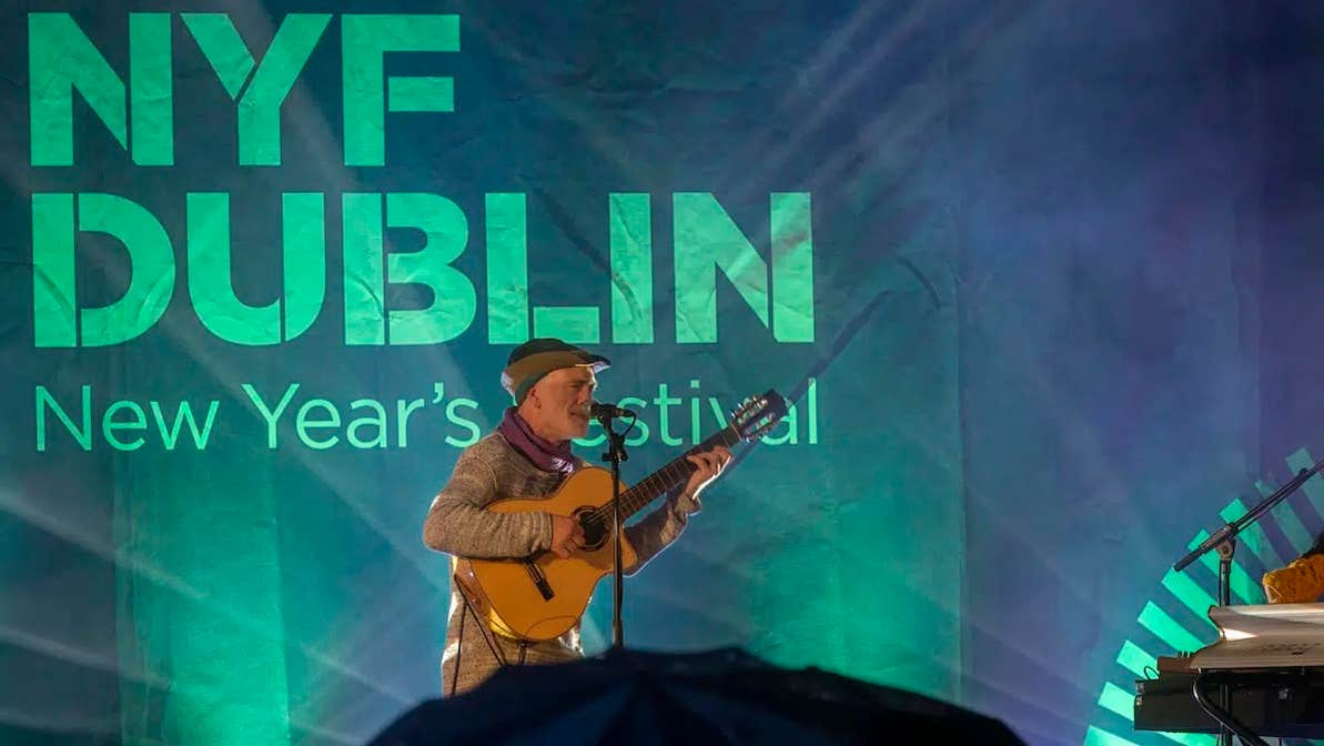 NYF Dublin, Traditional Music Concert - a man playing a guitar and singing on a stage, lit behind in green