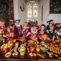 People in medieval costume posing at a table laid out with food and drink