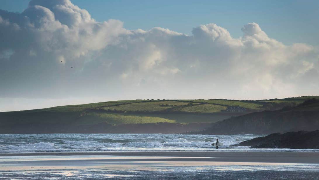 A surfer holding their surfboard watching the waves at Inchydoney beach in West Cork.