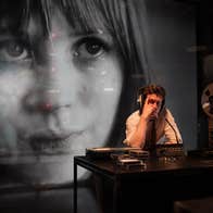 A man at a desk with audio equipment. An image of Marianne Faithful is being projected behind him.