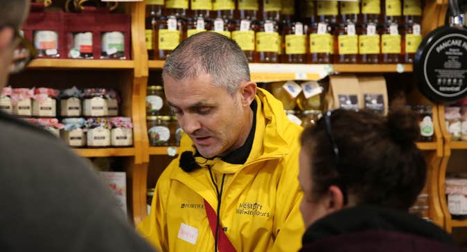 A tour guide discusses a food item with two people standing in foreground