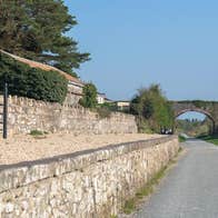 A walking path beside a stone wall continuing towards a stone bridge