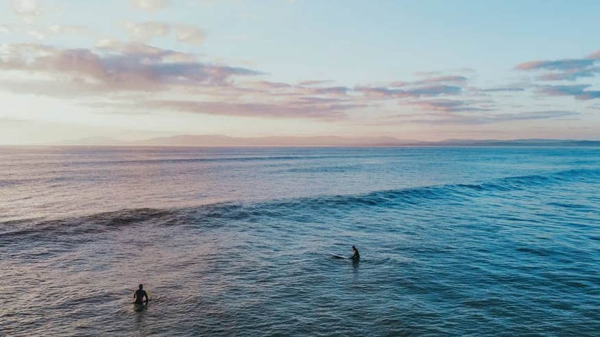 Two people surfing under pastel pink skies at Rossnowlagh Beach, Donegal