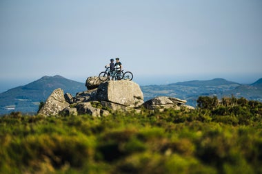 Two people with bicycles standing on a large rock overlooking the landscape