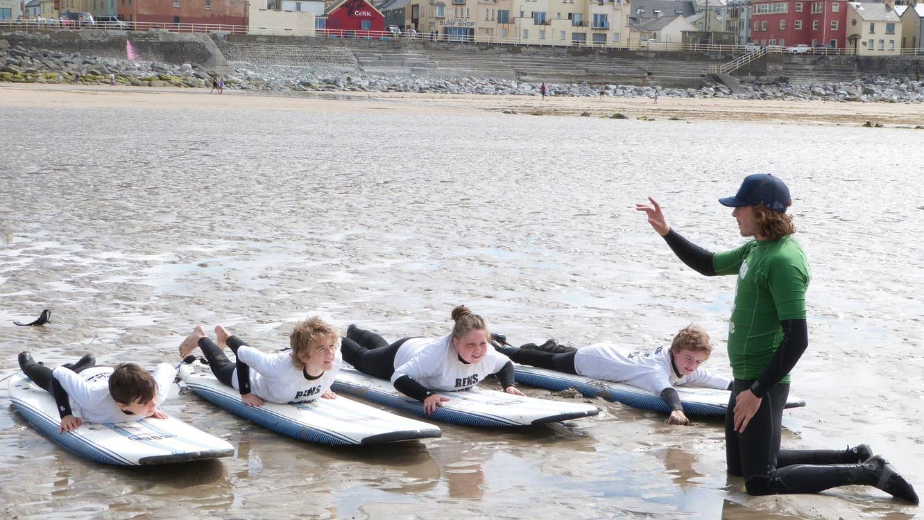 Four kids on surfboards on the stand with an instructor giving lessons