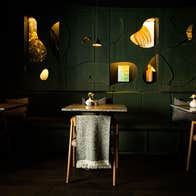 Three tables and chairs with grey scarfs on the back in a restaurant with dark green walls