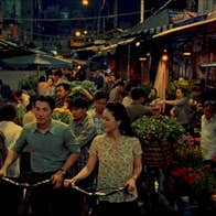 A man and a woman with bicycles are walking through a market.