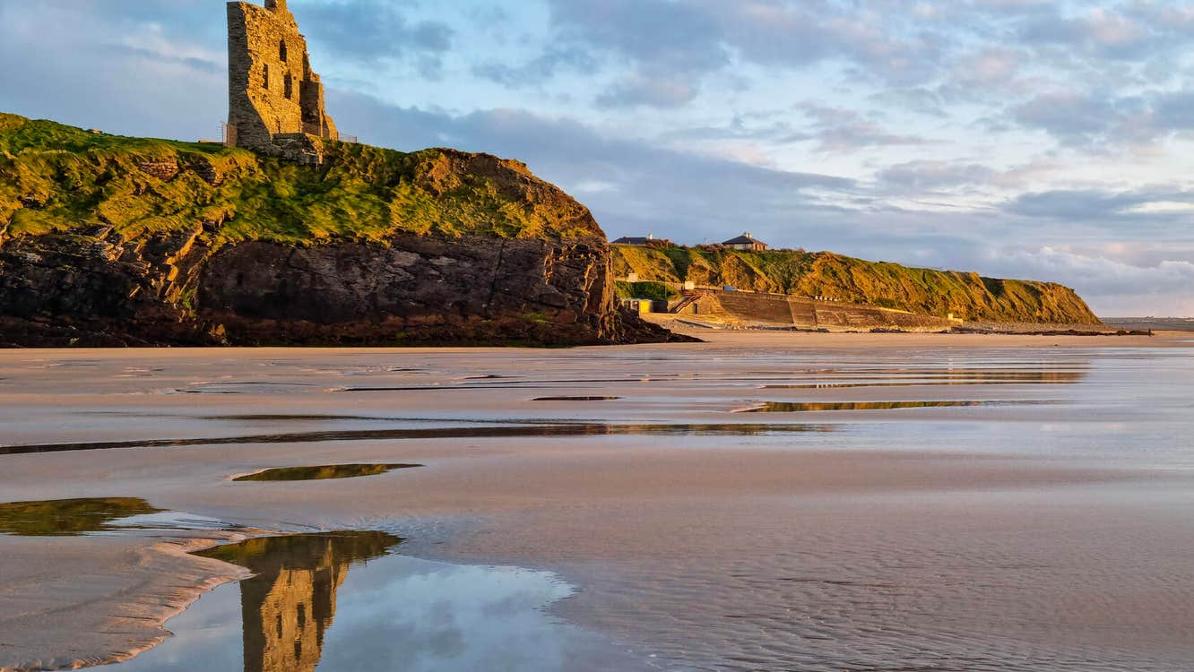 Ballybunion castle on cliff reflected in water on the beach below