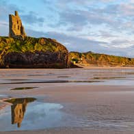 Ballybunion castle on cliff reflected in water on the beach below