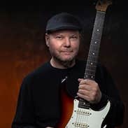 Christopher Cross, a man in a flat cap is holding upright an electric guitar.