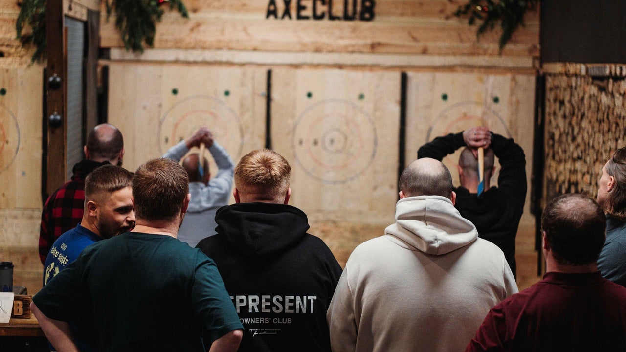 Two people throwing axes as a group of people watch